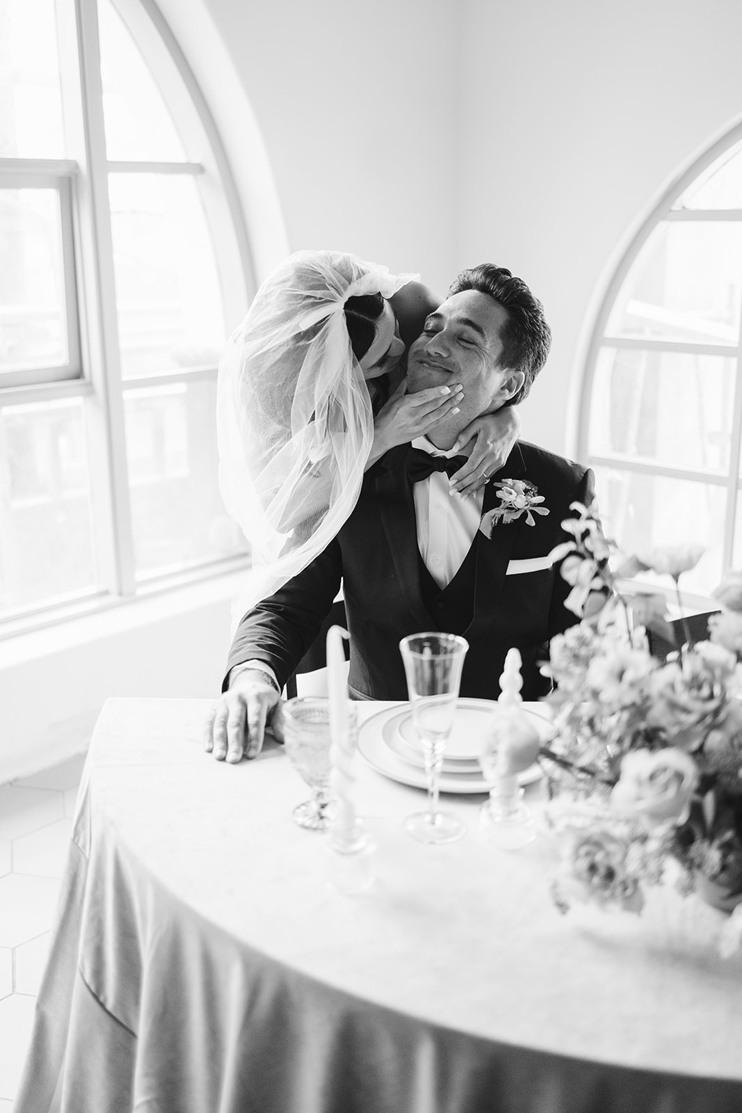 bride kissing groom's cheek as he sits at head table 