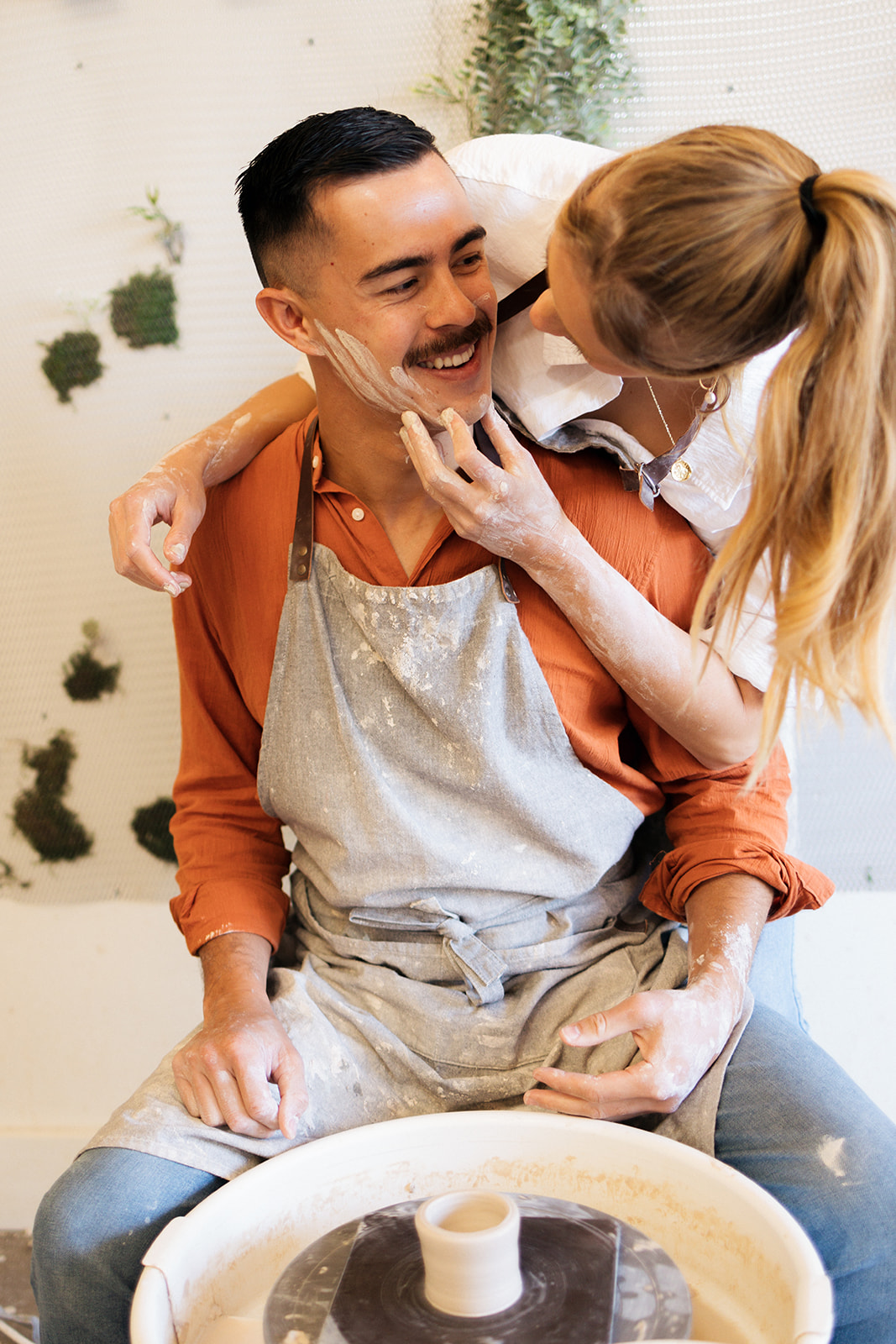 a couple smiling at each other as they make pottery 