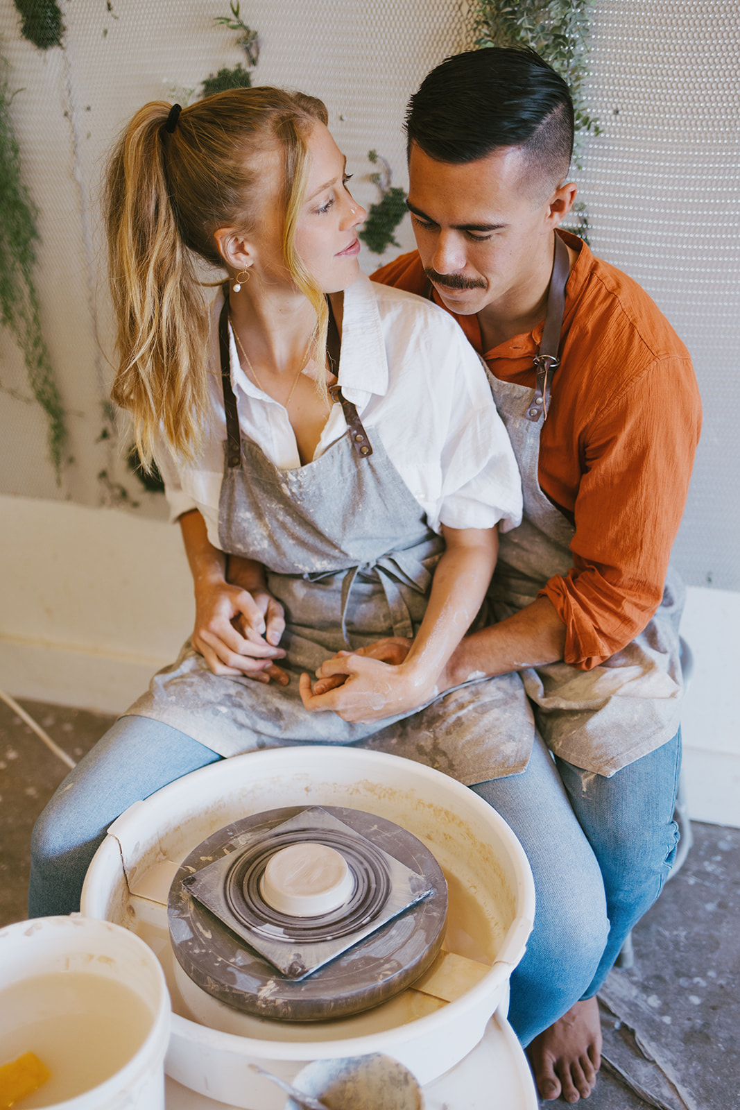 a couple sitting together at a pottery wheel during a date night photoshoot 