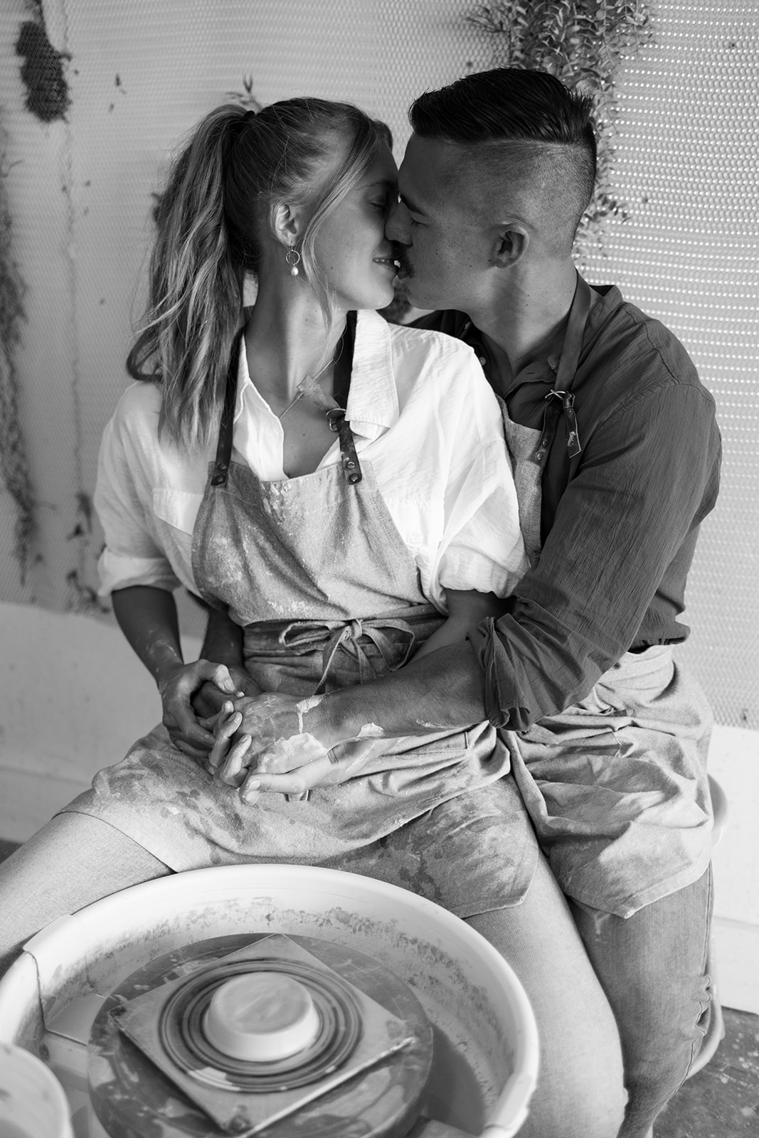 a couple kissing while at the pottery wheel during a date night photoshoot 