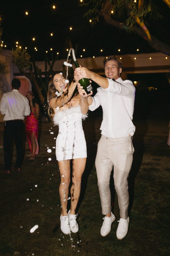 bride and groom popping a bottle of champagne 