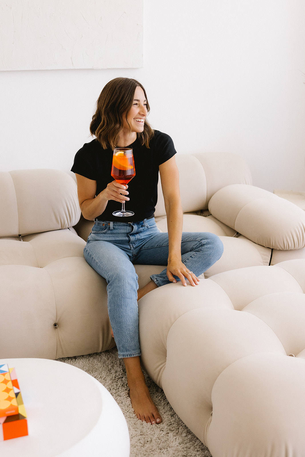 female business owner sitting on a couch with an aperol spritz during a brand photoshoot 