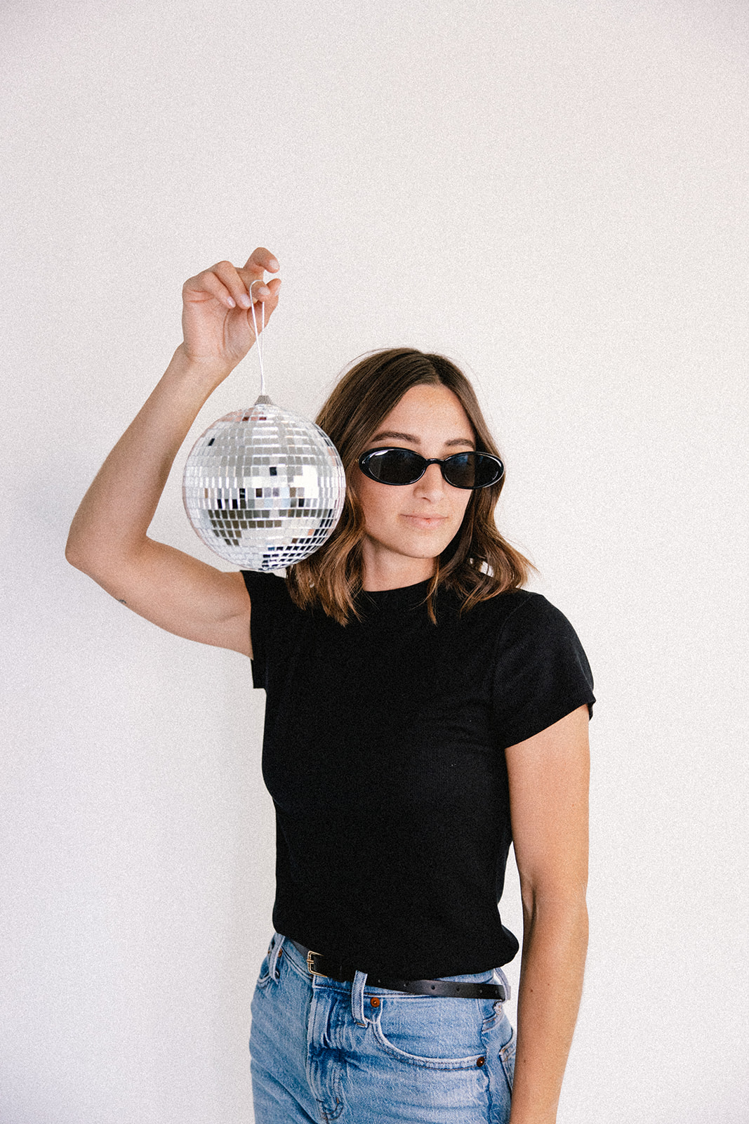 a woman in sunglasses holding up a disco ball for her studio branding photography session in Southern California