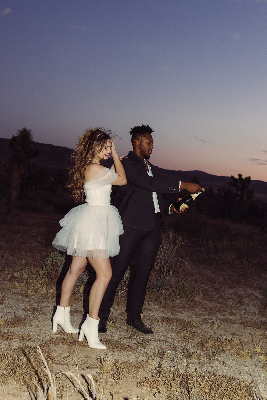 bride and groom popping champagne during sunset 