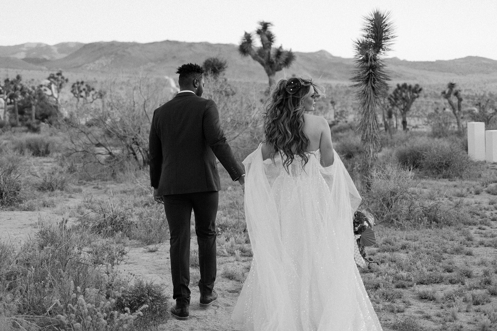 bridal couple with their backs to the camera as they walk through the park 