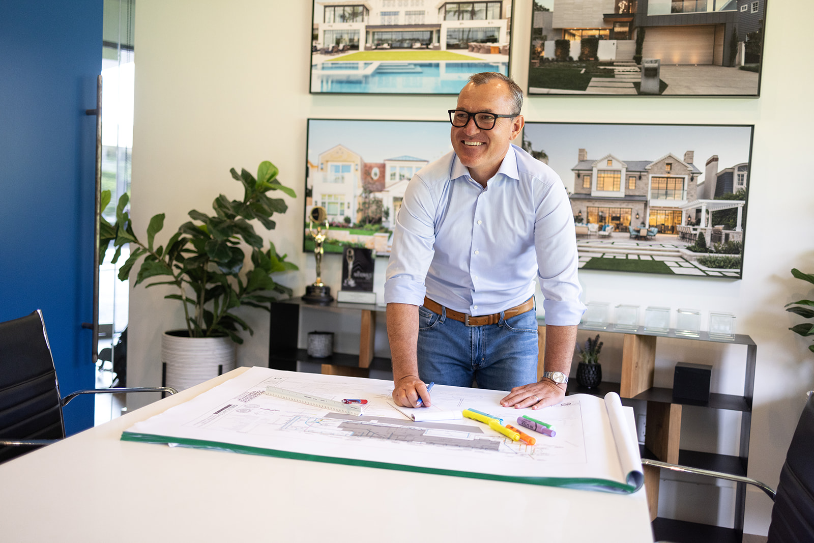 a man standing at the head of the table smiling as he works on business plans during a brand photoshoot