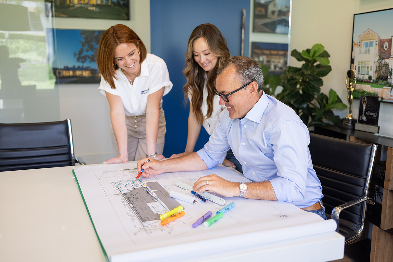 a man sitting and two women looking down at his plans during a California brand photoshoot