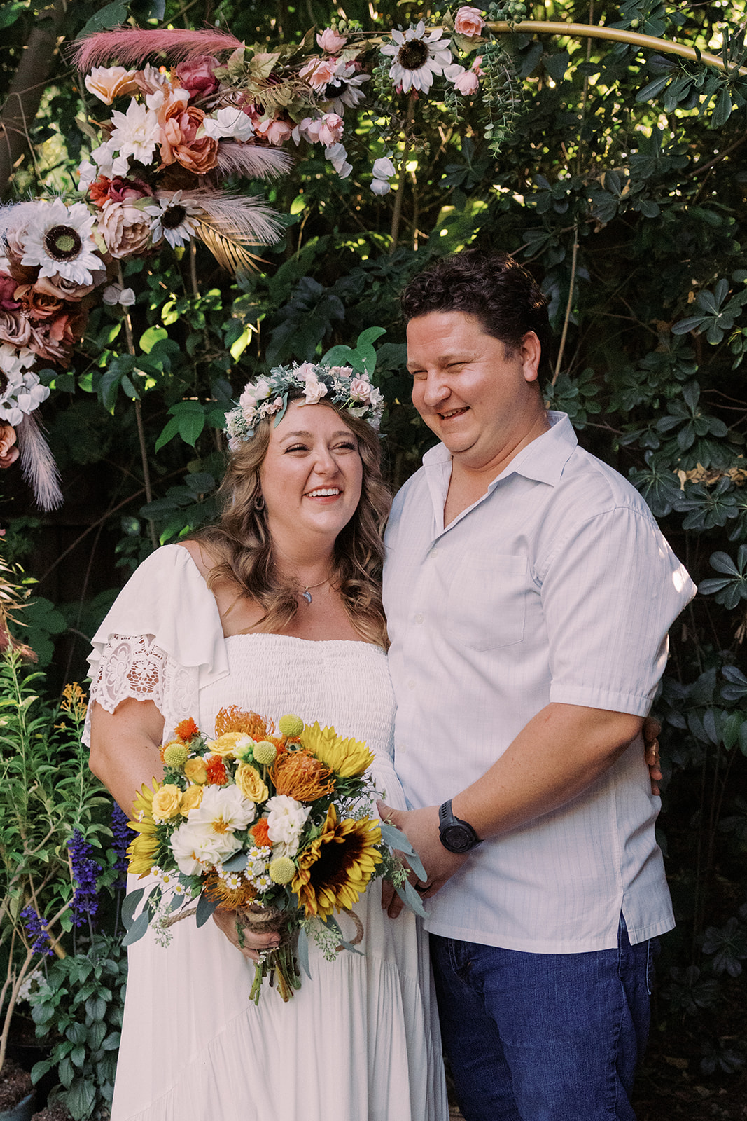 the bride and groom smiling underneath their floral altar 