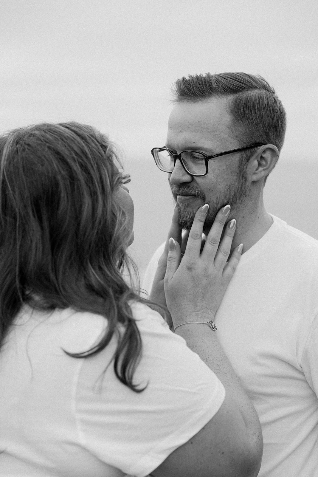 a woman holding a man's face as he looks her in her eyes during their beach engagement photos