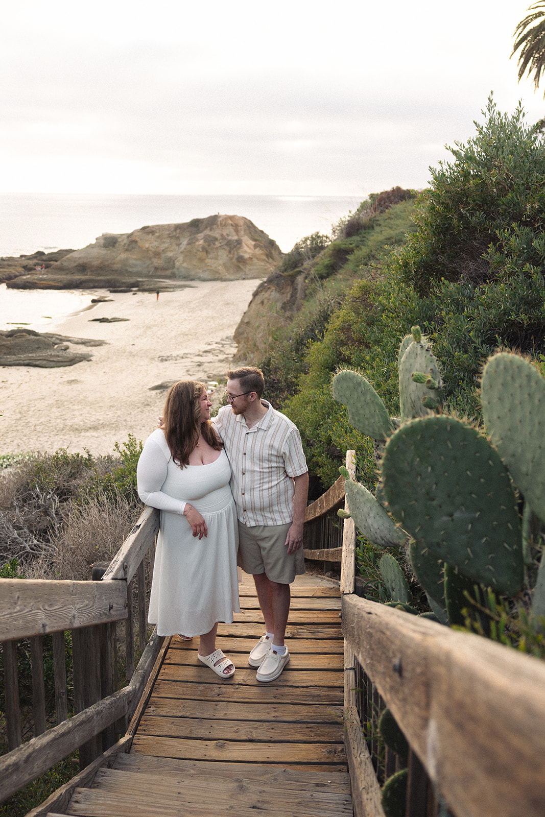 newly engaged couple standing on the stairs down to Laguna Beach 