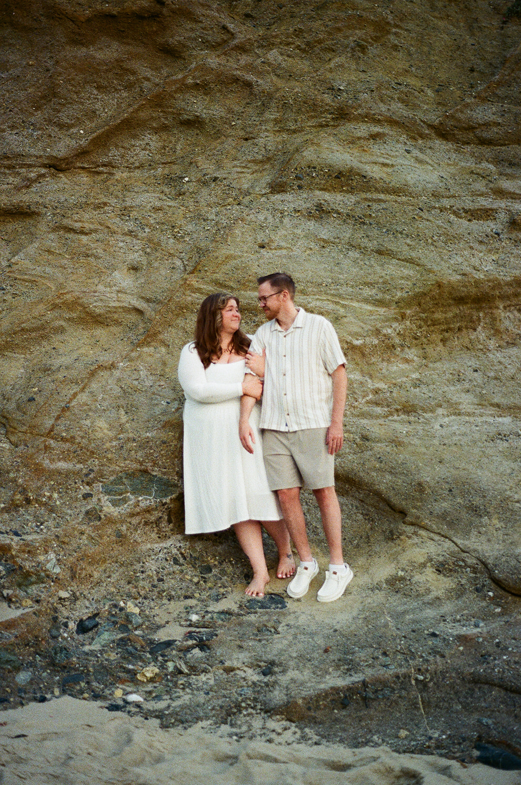 a couple standing by a rock wall during their film engagement photos at Laguna Beach 